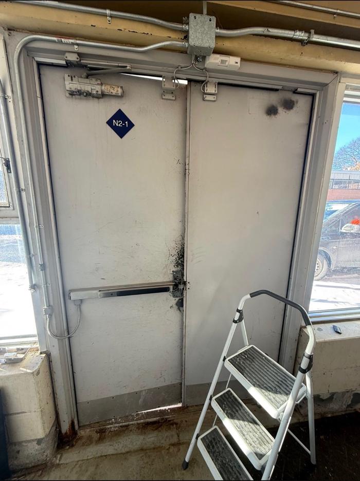 Before: close-up of the original steel double doors showing surface damage and deteriorated kick plates