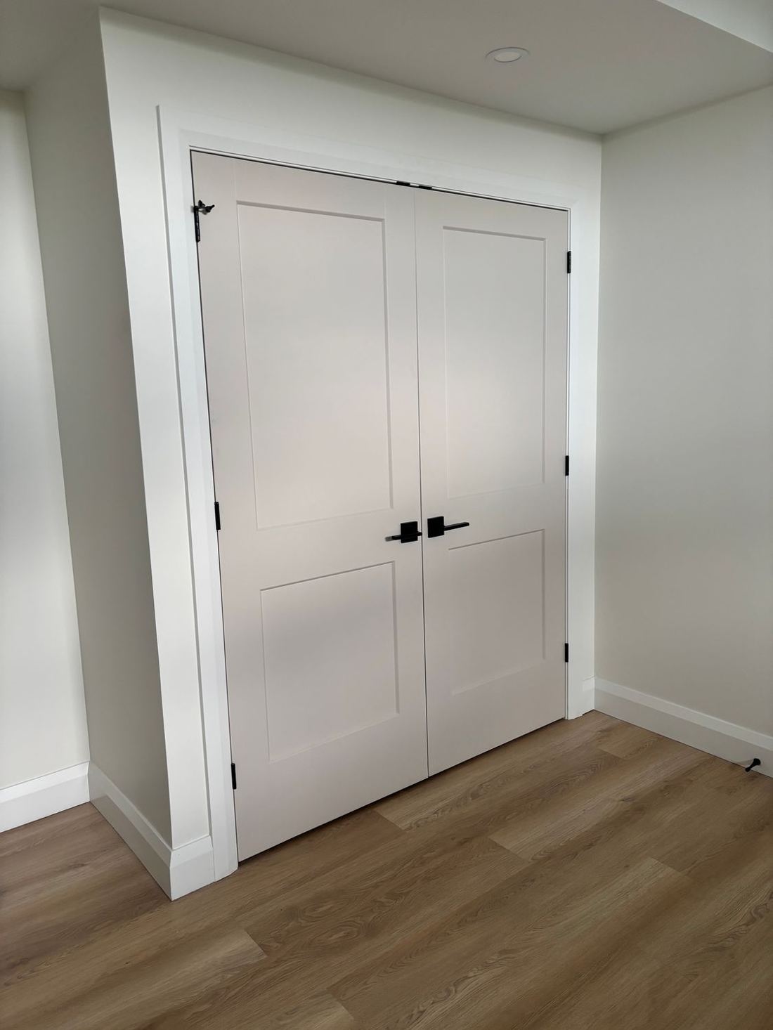 7 ft white shaker-panel closet doors with black handles installed over wood flooring in an Ottawa home