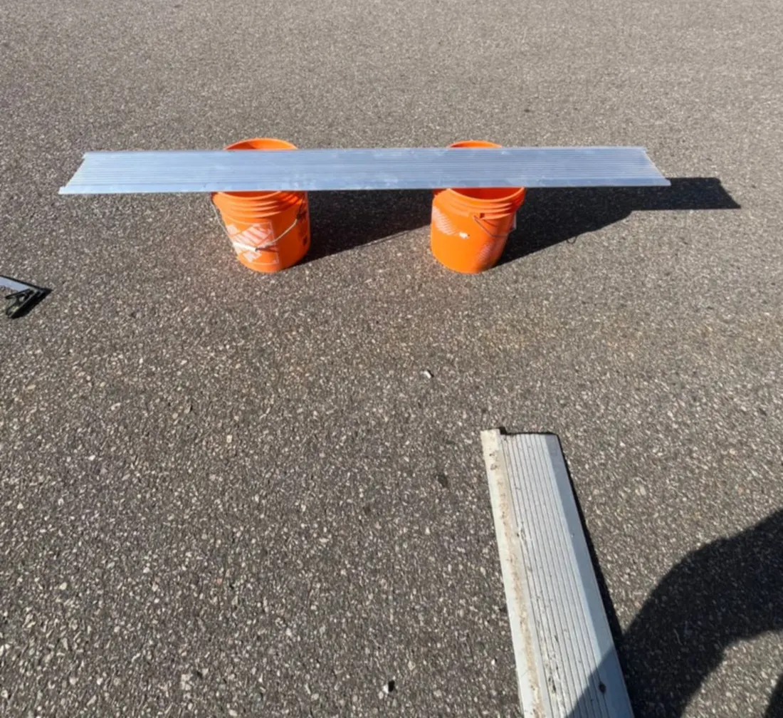 New fluted aluminum threshold laid across two buckets to be cut to length, with the old corroded threshold on the pavement beside it