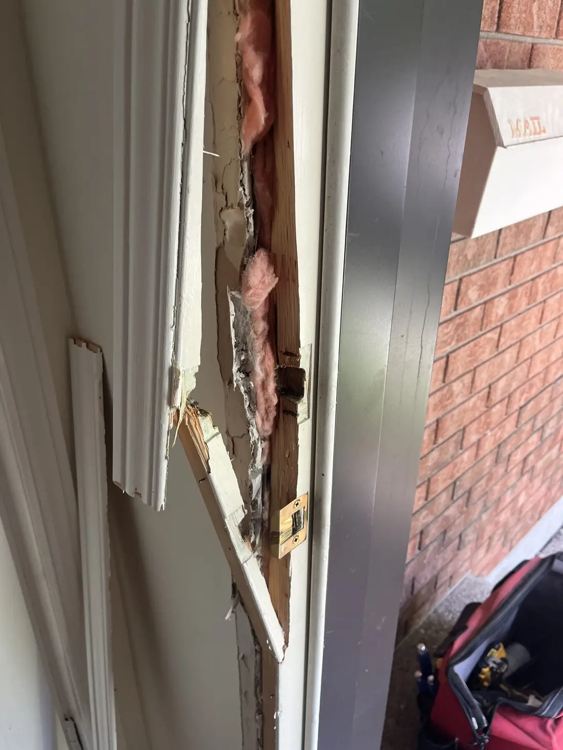 Before repair: Ottawa front door jamb split open around the deadbolt and latch strikes after forced entry, with insulation and broken trim exposed