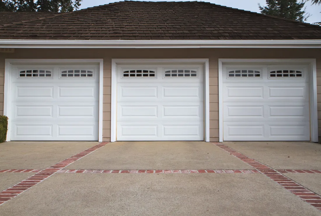 White raised-panel garage door sections on a brick-trimmed driveway