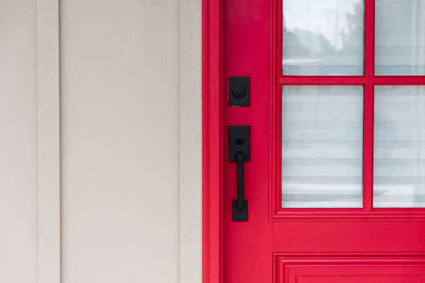 Close-up of a red entry door's black handleset and deadbolt beside divided-lite glass and cream siding