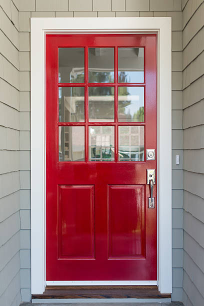 Glossy red nine-lite entry door in a white frame on a grey shingle-sided home